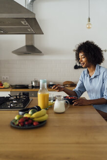 Frau frühstückt in ihrer Küche und isst Obst - BOYF01016