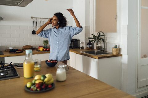 Frau tanzt und hört Musik am Morgen in ihrer Küche, lizenzfreies Stockfoto