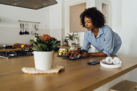 Frau mit digitalem Tablet und einem gesunden Frühstück in ihrer Küche, lizenzfreies Stockfoto