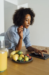 Woman using digital tablet and having a healthy breakfast in her kitchen - BOYF01057