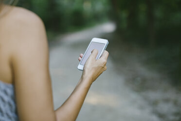 Woman using smartphone on forest track, partial view - MOMF00542