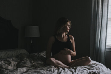 Schwangere Frau schaut weg, während sie zu Hause auf dem Bett sitzt - CAVF54563