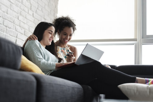 Niedriger Blickwinkel auf ein glückliches lesbisches Paar beim Online-Shopping, das zu Hause auf dem Sofa sitzt - CAVF54576