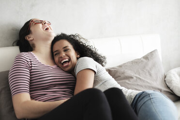 Happy lesbian couple laughing while relaxing on bed at home - CAVF54582