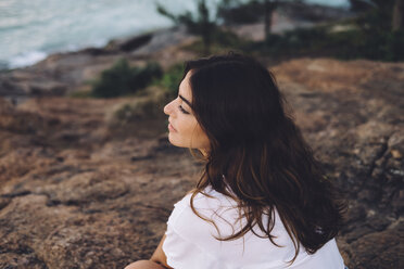 High angle view of thoughtful woman looking away while sitting on rock formation during sunset - CAVF54606