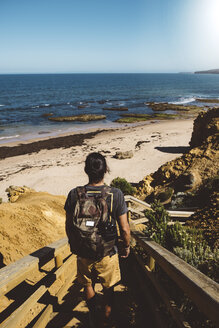 Rückansicht eines Mannes mit Rucksack, der auf den Stufen am Strand steht, gegen einen klaren blauen Himmel an einem sonnigen Tag - CAVF54607