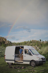 Man standing in motor home against cloudy sky at forest - CAVF54617