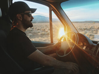 Seitenansicht eines selbstbewussten Mannes mit Sonnenbrille und Mütze beim Fahren eines Wohnmobils bei Sonnenuntergang - CAVF54621