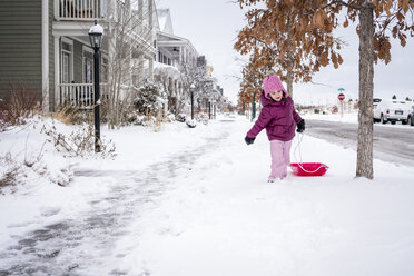Nettes Mädchen, das einen Schlitten zieht, während es auf einer schneebedeckten Straße spazieren geht - CAVF54636