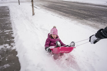 Cropped hand of father pulling daughter sitting in sled on snow covered road - CAVF54637