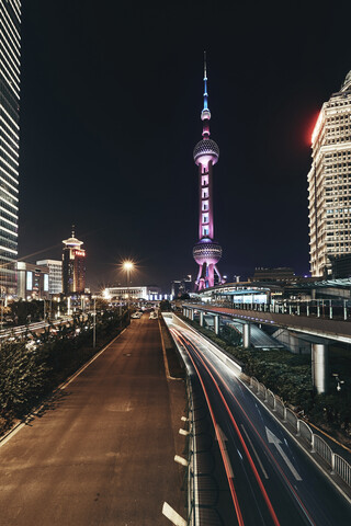 Lichtspuren auf der Straße gegen den beleuchteten Oriental Pearl Tower in der Stadt bei Nacht, lizenzfreies Stockfoto