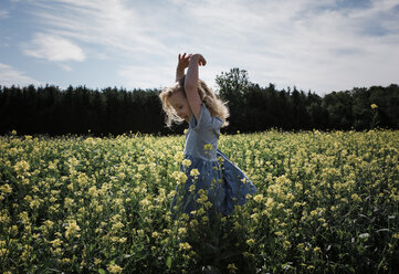 Happy girl with arms raised standing amidst plants against sky - CAVF54673