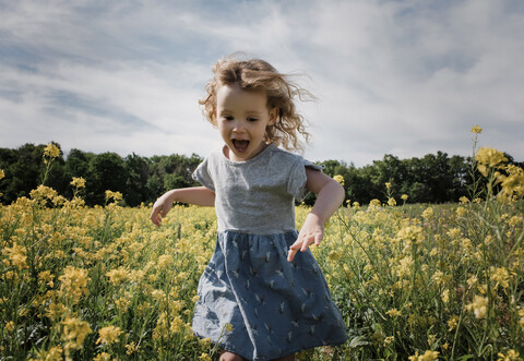 Glückliches Mädchen läuft stehend inmitten von Pflanzen gegen bewölkten Himmel, lizenzfreies Stockfoto