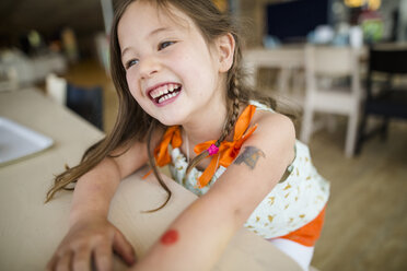 Close-up of happy girl looking away while sitting by wooden table at home - CAVF54683