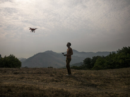 Seitenansicht eines Mannes, der eine Drohne per Fernsteuerung gegen Berge steuert - CAVF54722