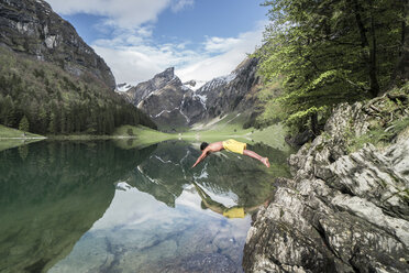 Side view of shirtless man diving into lake against mountains - CAVF54725