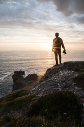 Rückansicht der Silhouette Mann mit Kamera stehen auf Klippe am Strand gegen bewölkten Himmel bei Sonnenuntergang - CAVF54743