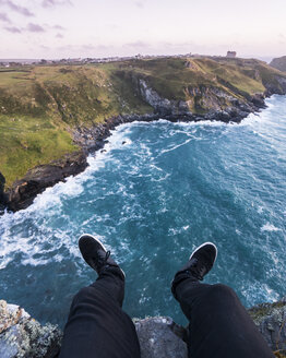 Niedriger Ausschnitt eines auf einer Klippe am Meer sitzenden Mannes gegen den Himmel - CAVF54745
