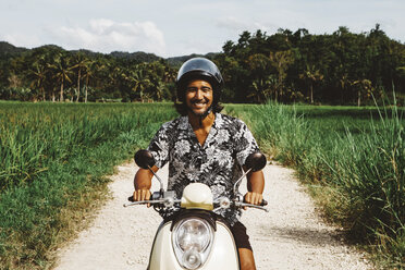 Porträt eines lächelnden Mannes, der auf einem unbefestigten Weg gegen den Himmel Motorrad fährt - CAVF54758
