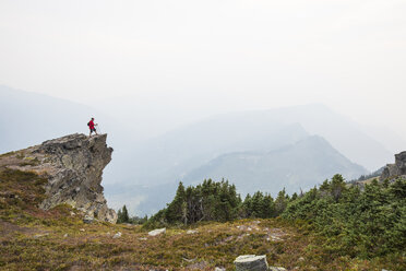 Wanderer in voller Länge auf einer Klippe stehend gegen Berge und Himmel bei nebligem Wetter - CAVF54768