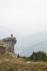 Side view of hiker standing on cliff against mountains and sky during foggy weather - CAVF54769