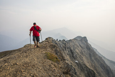 Wanderer in voller Länge mit Wanderstöcken beim Wandern auf einem Berg gegen den Himmel - CAVF54770