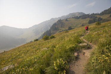 Blick aus der mittleren Entfernung auf einen Wanderer, der auf einem Weg inmitten eines Feldes gegen Berge läuft - CAVF54771