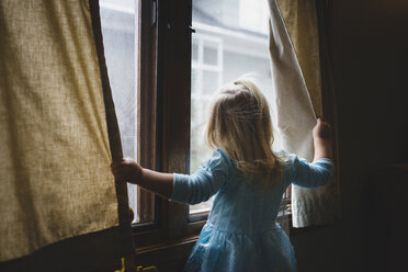 Rückansicht eines Mädchens, das durch ein Fenster schaut, während es zu Hause steht - CAVF54776
