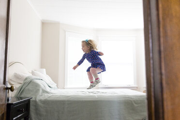 Seitenansicht eines glücklichen Mädchens, das zu Hause auf das Bett springt - CAVF54777