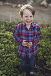 Ganzkörperporträt eines fröhlichen Jungen inmitten von Pflanzen im Park - CAVF54784
