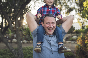 Portrait of cheerful father carrying son on shoulders while playing with him at park - CAVF54788