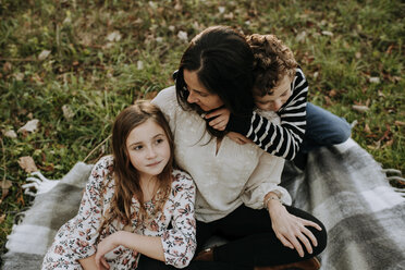 High angle view of brother embracing mother while sister sitting by her on picnic blanket at park - CAVF54800