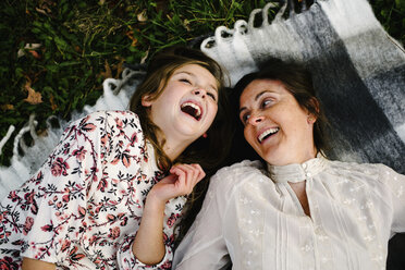 High angle view of cheerful mother and daughter lying on picnic blanket at park - CAVF54801