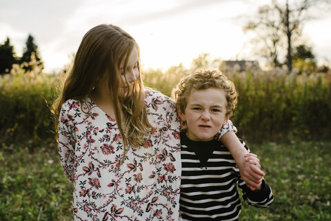 Porträt eines Bruders, der neben seiner Schwester im Park steht und ein Gesicht macht, lizenzfreies Stockfoto