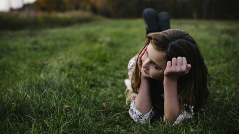 Nachdenkliches Mädchen liegt auf einer Wiese im Park, lizenzfreies Stockfoto