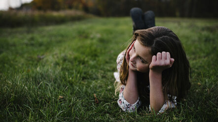 Thoughtful girl lying on grassy field at park - CAVF54803