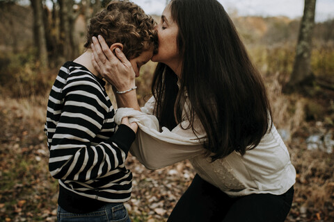 Seitenansicht der Mutter, die den Kopf ihres Sohnes im Park küsst, lizenzfreies Stockfoto