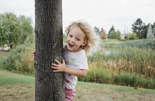 Porträt eines niedlichen glücklichen Mädchens, das an einem Baum im Park steht - CAVF54821