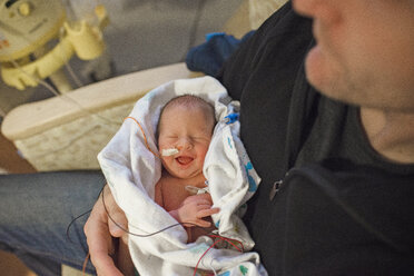 Hochformatiger Mittelteil eines Vaters mit neugeborenem Sohn, der auf einem Stuhl im Krankenhaus sitzt - CAVF54824