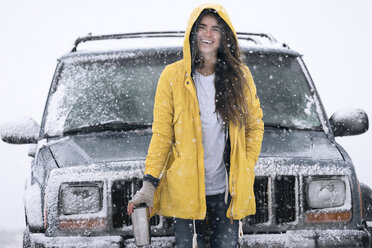 Porträt einer fröhlichen Frau, die neben einem Geländewagen auf einem Feld im Winter steht - CAVF54828