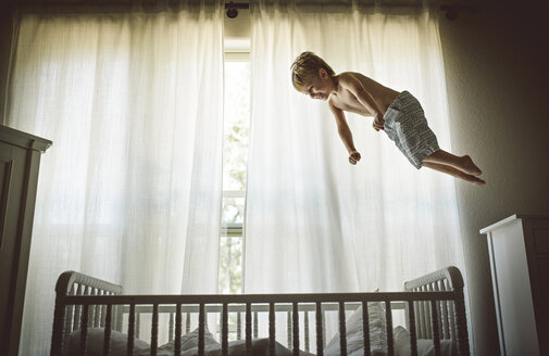 Hemdloser Junge schwebt über Krippe gegen Fenster zu Hause - CAVF54830