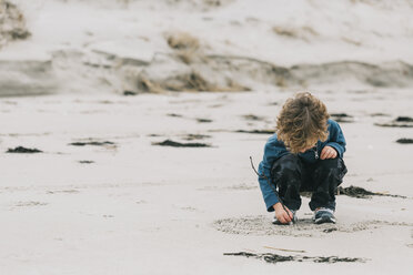 Boy writing on sand while crouching at beach - CAVF54834