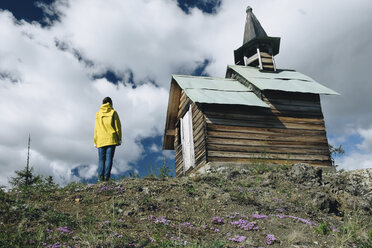 Rückansicht einer reifen Frau, die an einer Kirche auf einem Hügel steht, gegen einen bewölkten Himmel - CAVF54835