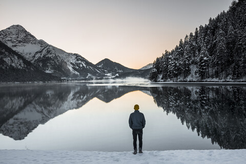 Rückansicht eines Mannes am Seeufer gegen den Himmel im Winter, lizenzfreies Stockfoto