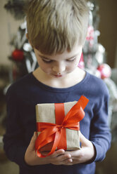 Junge mit Geschenk in der Hand vor dem Weihnachtsbaum zu Hause - CAVF54857