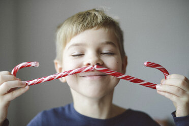 Verspielter Junge macht Schnurrbart mit Zuckerstangen zu Hause - CAVF54858