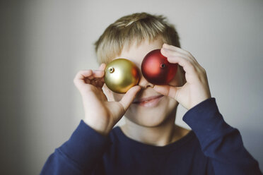 Playful boy holding baubles against face at home - CAVF54864