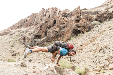 Full length portrait of backpacker screaming while balancing on rocks at desert - CAVF54874