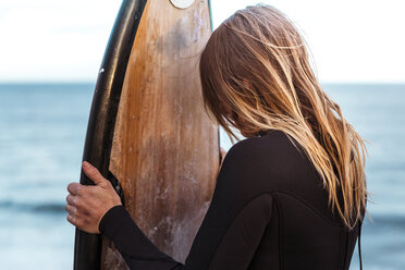 Frau trägt Neoprenanzug und hält Surfbrett am Strand - CAVF54882