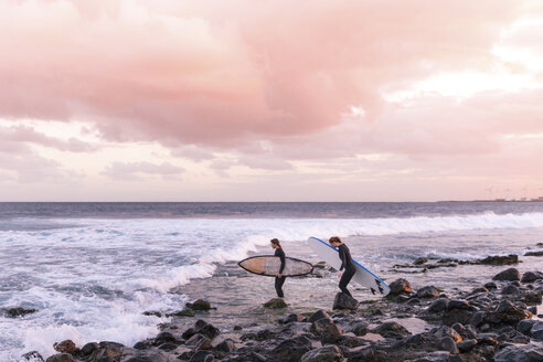 Female friends carrying surfboards on shore at beach against cloudy sky - CAVF54884